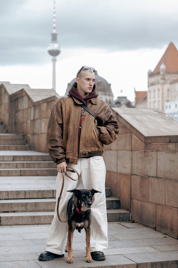 Männliches Model sthet in Berlin, im Hintergrund der Fernsehturm, mit seinem Hund. In der Hand hält er seine Leine in braun von SUNNY BERLIN